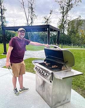A man is grilling food on a barbecue in a backyard.