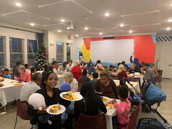 A group of people are sitting at tables in a room with a Christmas tree in the background.