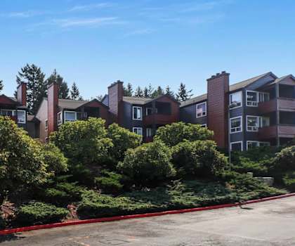 Apartment complex with red trim and green bushes in front.