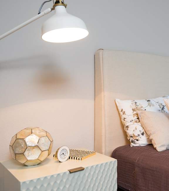A bedroom with a bed, a nightstand with a lamp, and a soccer ball on the nightstand.