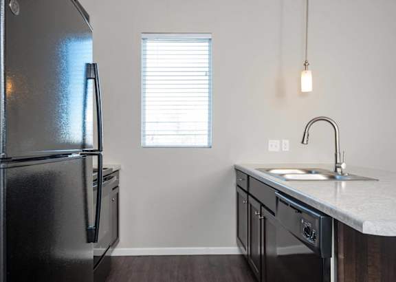 A black refrigerator is in a kitchen with a sink and a window.