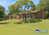 Thumbnail 5 of 7 - A large grassy field in front of a brick building with a tree in the middle.