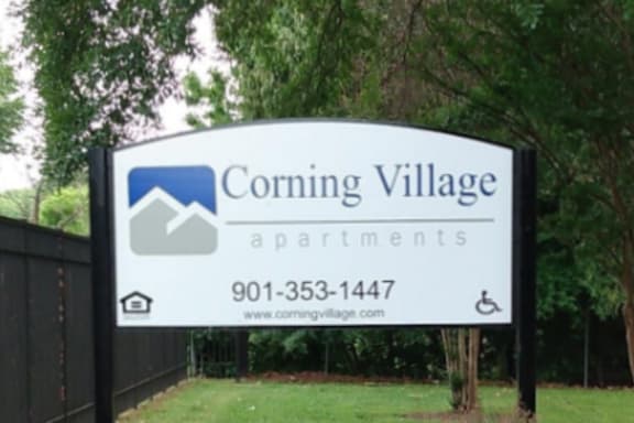 A sign for Corning Village Apartments with a phone number and website.