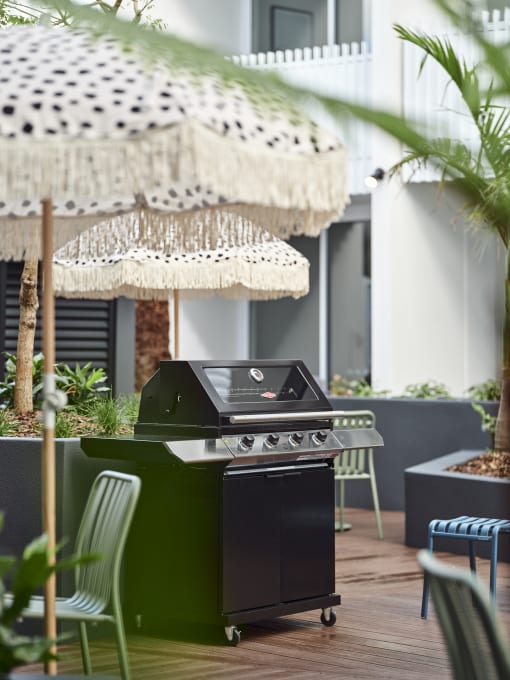 a barbecue grill on a patio with chairs and umbrellas