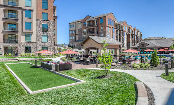 a grassy area with umbrellas and tables and chairs in front of an apartment building  at EdgeWater at City Center, Lenexa, KS, 66219