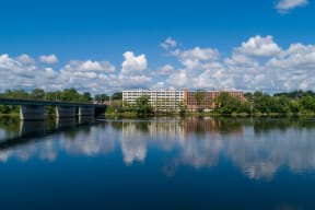 A large building is reflected in the water in front of it. at Montgomery Mill Apartments in Windsor Locks, CT