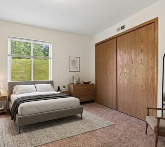 A bedroom with a large bed, a nightstand with a lamp, a chair, and a wooden wardrobe.