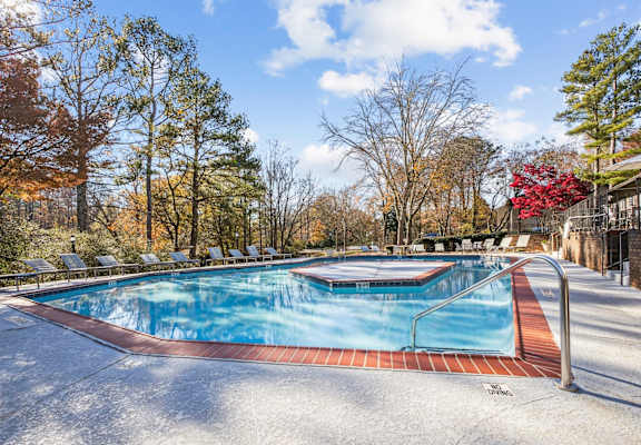A pool surrounded by trees in a sunny day at Riverwood Crossing apartments in Roswell, GA.