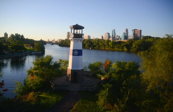 a lighthouse in front of a river with a city in the background
