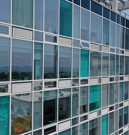 A modern building with large glass windows reflecting the sky and other buildings.