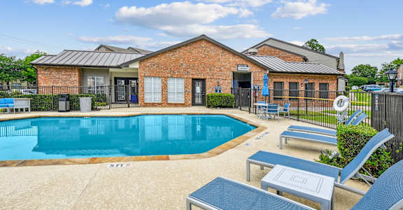 A pool with a blue lounge chair and a brick building in the background.