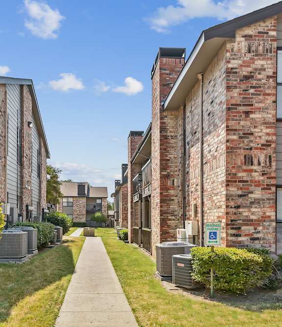 a pathway between two brick apartment buildings with grass and trees
