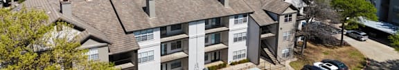 An apartment building with a parking lot and covered parking spots at Jefferson Place Apartments in Irving, TX