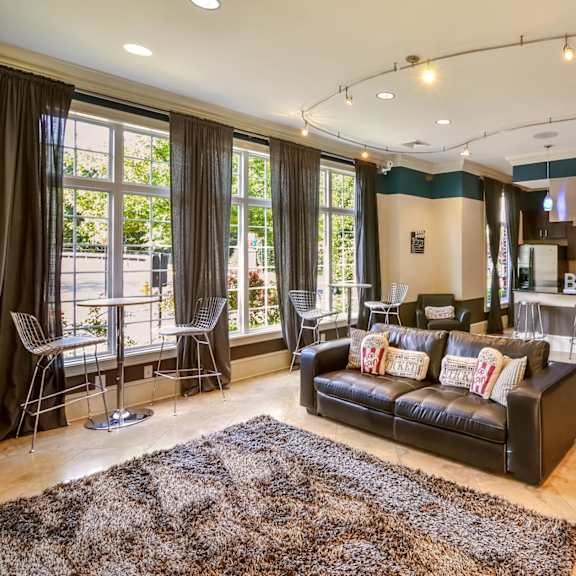 A modern living room with a black couch and a kitchen area in the background.