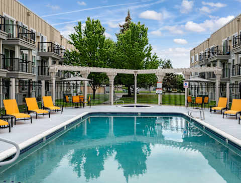 A swimming pool surrounded by orange lounge chairs and a white pergola.