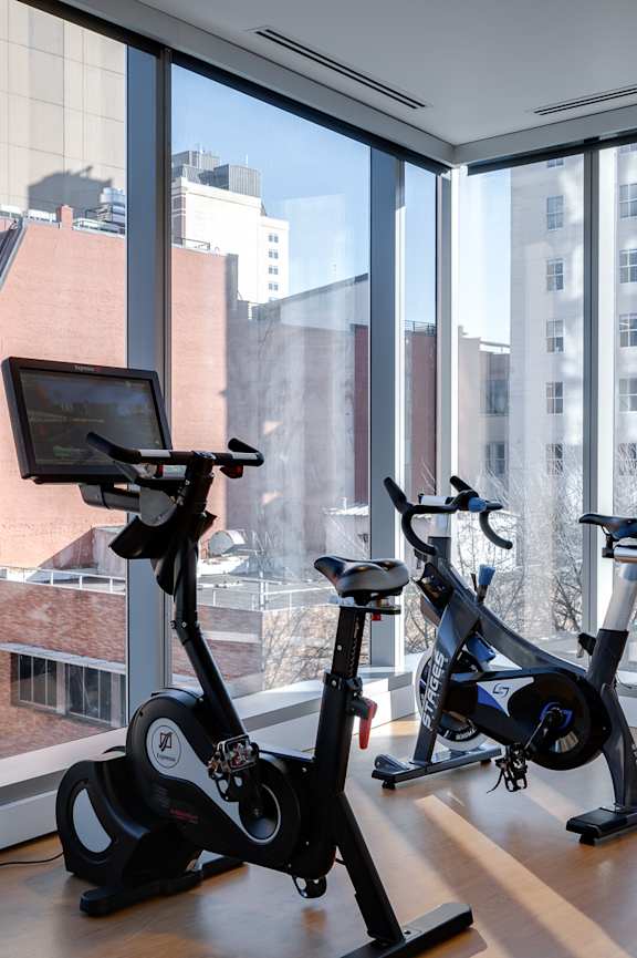 Two exercise bikes are placed in front of a window with a view of the city.