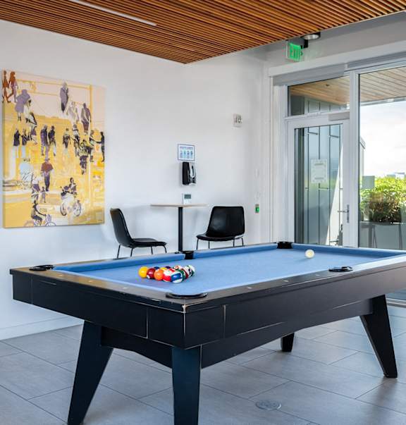 2-Bedroom Apartments in Pearl District, Portland, OR - Couch9 - Residential Lounge with Tile Flooring, Billiards Table, High-Top Table and Chairs, Glass Door, and Floor-to-Ceiling Windows.