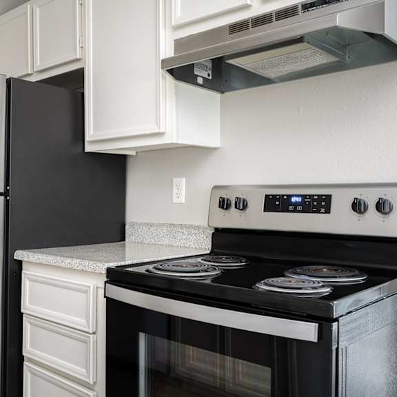 A black stove top oven with a digital display and a silver refrigerator in a kitchen.