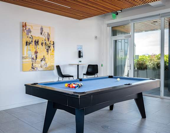 2-Bedroom Apartments in Pearl District, Portland, OR - Couch9 - Residential Lounge with Tile Flooring, Billiards Table, High-Top Table and Chairs, Glass Door, and Floor-to-Ceiling Windows.