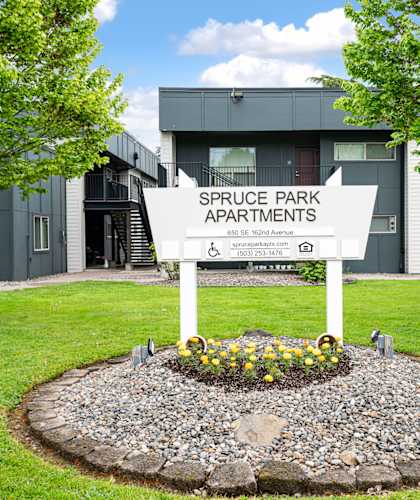 A sign for Spruce Park Apartments is in front of a grey building.