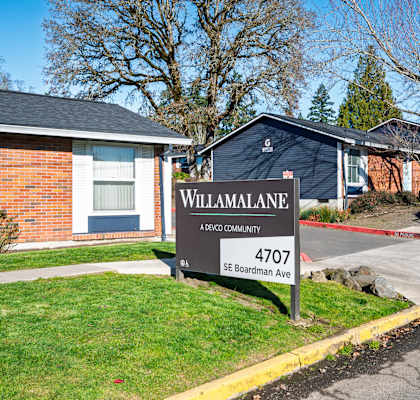 A sign for Willamalane Apartments stands in front of a brick house.