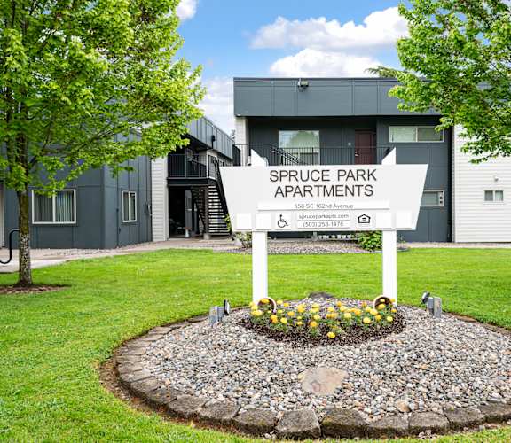 A sign for Spruce Park Apartments is in front of a grey building.