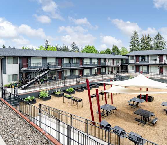 A courtyard with tables and chairs surrounded by a fence and apartment buildings.
