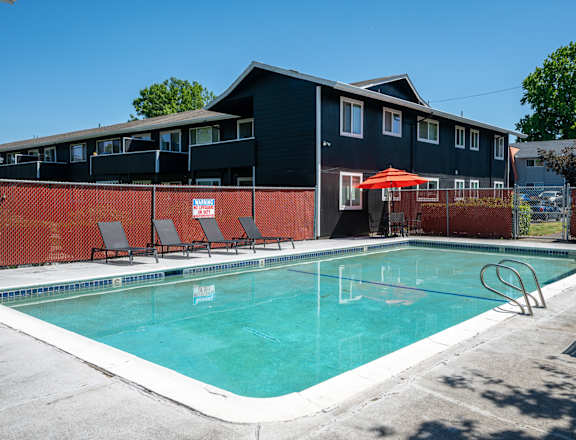 A swimming pool in front of a building with a red umbrella.