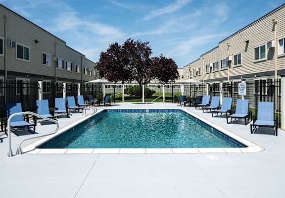 A swimming pool surrounded by chairs and a tree in the middle of a courtyard.