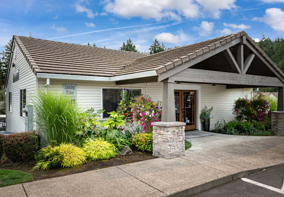 A house with a white exterior and a brown roof with a stone pillar in front.