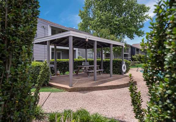 A pavilion with a picnic table is surrounded by greenery.