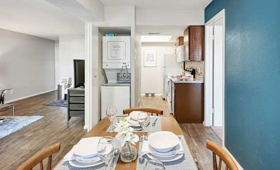 a dining area with a wooden table and chairs and a kitchen in the background