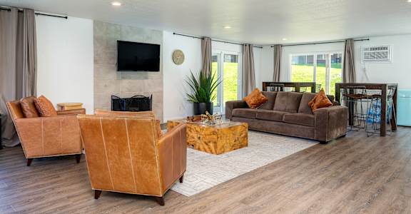 A living room with a brown sofa, a yellow ottoman, and a flat screen TV mounted on the wall.