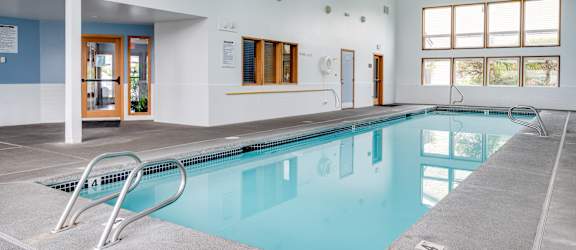 a swimming pool in a large room with a pool table and chairs