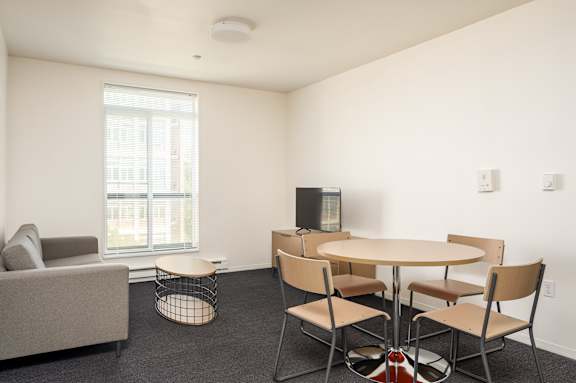 A living room with a grey couch, a round table with four chairs, and a television.