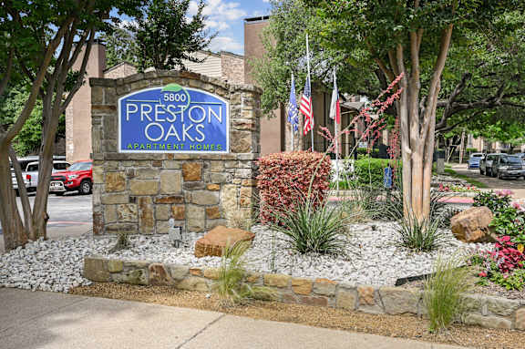 A sign for Preston Oaks Apartment Homes is displayed in front of a landscaped area.