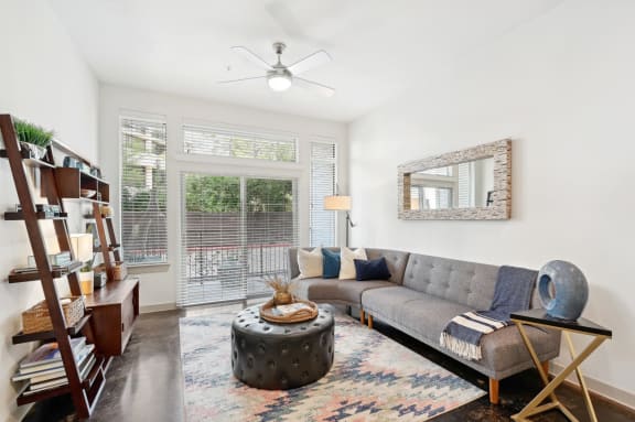 Model living room with a couch and a coffee table and a kitchen in the background at Harlow River Oaks in Houston, TX