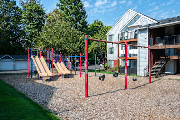 A playground with a red swing set and a slide.