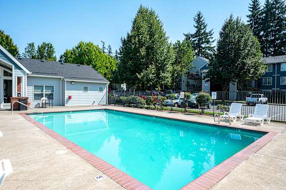A swimming pool surrounded by a concrete patio and a black fence.