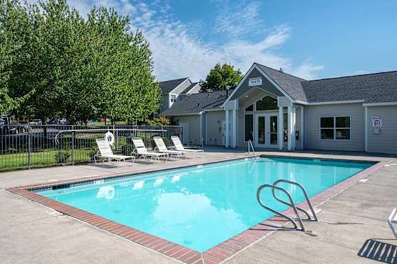 A pool with a diving board and lounge chairs in front of a building.