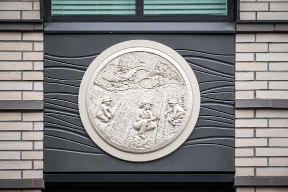 A circular stone plaque with carved figures is mounted on a wall.