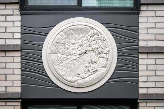 A circular relief sculpture of a man and a woman is mounted on a dark wall.