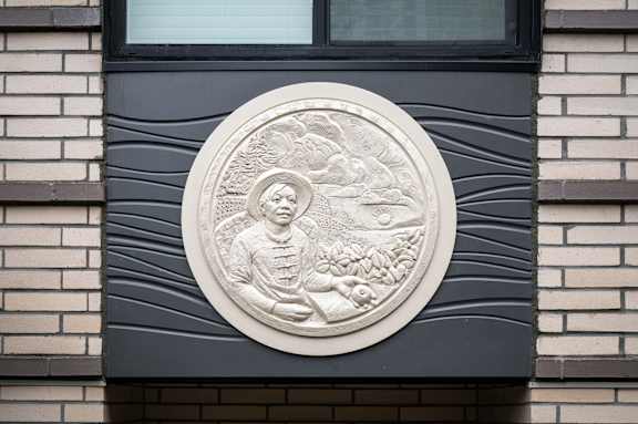 A circular stone carving of a person holding a plant is mounted on a dark wall.