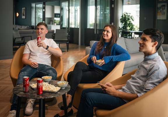 Three people are sitting in a circle on chairs and eating popcorn.