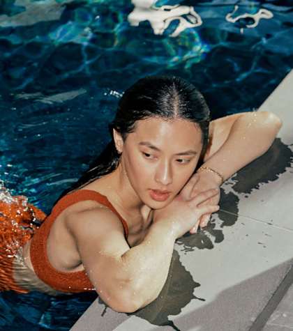 A woman in an orange swimsuit is swimming in a pool.