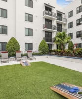 Grassy courtyard with lounge chairs, a cornhole game, and a modern apartment building in the background at Bay Village 1 Apartment in Palmetto Bay, FL