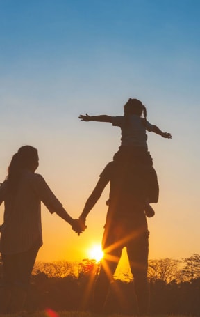 a man and woman holding hands with a child on their shoulders as the sun sets in the