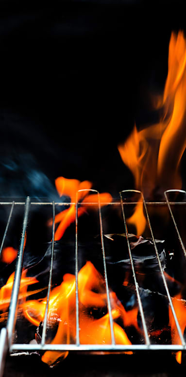 A close up of a grill with flames and smoke rising from it.