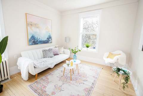 A living room with a white couch, a painting on the wall, a white chair, and a rug on the floor.