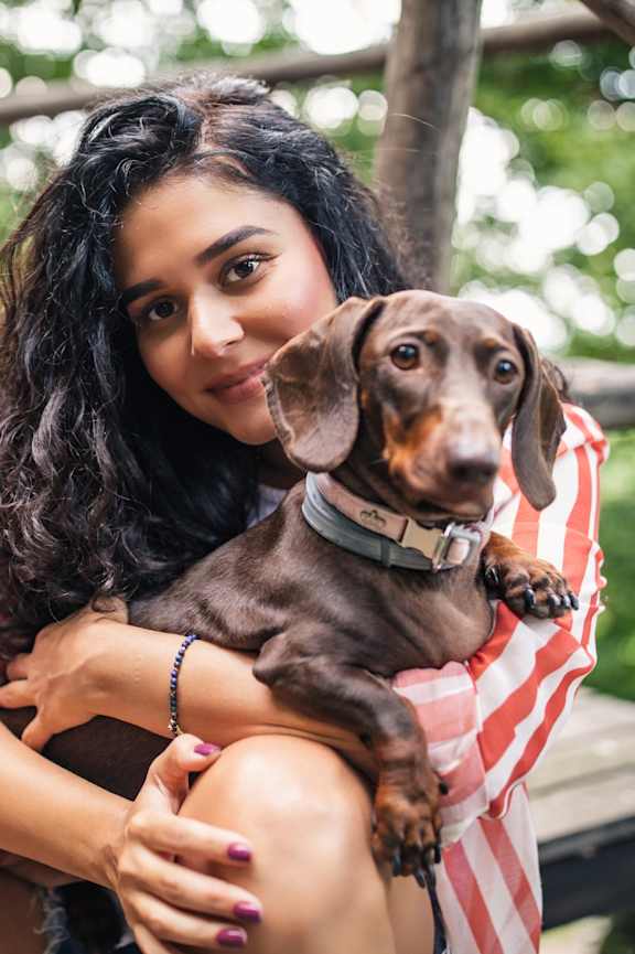 A woman is sitting on a wooden platform holding a brown dachshund.